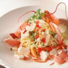 Plat de spaghetti au homard garni de chair de homard, copeaux de parmesan et herbes fraîches, présentation gastronomique.