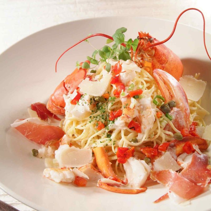 Plat de spaghetti au homard garni de chair de homard, copeaux de parmesan et herbes fraîches, présentation gastronomique.